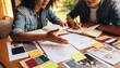 © Future Vision - Pointing two designers wearing denim reviewing sketches while writing at window table with swatches