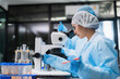 © VStudio - Asian female scientist team in cleanroom suit using microscope for medical research in laboratory. Commercial biotech pharmaceutical business and health innovation for sustainable development.