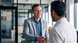 © Athena Studio - Smiling young businessman shaking hands with a colleague or client in a modern office setting, signifying agreement.