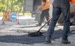 © Сергей Иванкин - Road construction worker using a rake to level fresh asphalt with warning traffic signs in the background
