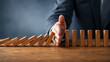 © Ishan - Businessman stopping domino effect to protect company stability and risk management strategy during financial crisis and business disruption prevention