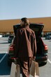 © Andrii Zastrozhnov - Man carrying paper shopping bags toward open car trunk outside store for shopping lifestyle background and banner