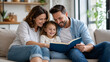 © GrayFrog - Happy family with little daughter smiling and reading a book together while sitting on a comfortable sofa at home.