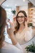 © thodonal - Young woman trying on stylish glasses in optical store mirror
