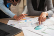 © NewSaetiew - Business Women Analyzing Financial Reports and Accounting Data with Charts, Graphs and Coins on Office Desk During Budget Planning Meeting.