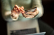 © Davor - Person using smartphone over laptop at home
