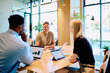 © we.bond.creations - Diverse business professionals discussing data and strategy during a meeting, smiling and cooperating in a modern office setup