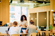 © we.bond.creations - Diverse business team collaborating and discussing a project in a bright open-plan office space. Woman manager presenting to colleagues