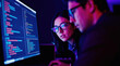 © Pete - Two people analyze code on computer screen. One woman wears glasses, looking intently at monitor. Team works late, illuminated by screen light.