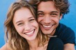 © Natalia - Stylish young interracial couple smiling and embracing against a vibrant blue background, showcasing their joyful connection and modern fashion choices
