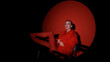© ekaterinabyuksel - Portrait of a beautiful young woman in a red fur coat against a red background, posing for a cinema-style photo. The woman smiles beautifully, sitting on chairs in the light of a projector during a