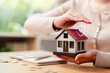 © Kiattisak - Home insurance, real estate protection and mortgage concept. Woman hands protecting miniature house model with safety shield icon, coins and calculator.