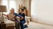 © Mr. Bolota - Caregiver helping elderly woman put on cardigan in bedroom