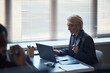 © DragonImages - Middle aged Caucasian businesswoman working on laptop during office meeting, reviewing documents and discussing strategy. Ideal for leadership, management, consulting, corporate planning