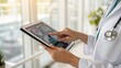 © thanawat - Doctor examining brain scans on a digital tablet in a bright medical office with a stethoscope visible.