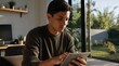 © Imaginary - Young Man Using Digital Tablet at Home Near Window with Garden View