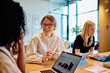 © we.bond.creations - Diverse businesswomen collaborating and having a discussion in a bright office, working on laptops and tablets