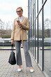 © LIGHTFIELD STUDIOS - Elegant woman in stylish attire checking her phone outside a modern building