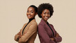 © Kiozmedias.fr - Deux femmes d'affaires noires confiantes debout dos à dos, bras croisés, portant des blazers professionnels sur fond beige neutre