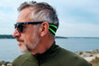 © Mediaphotos - Close up of senior man wearing sports sunglasses and headband, standing by coastline and looking away, conveying active aging and wellness. Ideal for fitness or lifestyle marketing