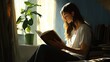 © Zeva - Woman reading book by window, lit by sunlight, home interior