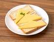 © Fatin - Delicious and simple breakfast toast with triangular yellow cheese slices and fresh parsley garnish, served on a white plate atop a warm wooden table, perfect for a quick snack or morning meal