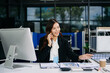 © Nuttapong punna - Professional Asian businesswoman talking on smartphone while working in modern office, corporate communication and productivity concept.