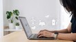 © Wei - Woman working on laptop with sustainable energy interface, solar panel and wind turbine icons, remote work from home concept