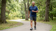 © Xenia - Active senior African American man walking briskly on a paved path in a green park. Older male exercising outdoors for cardiovascular health and fitness