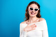 © deagreez - Smiling young woman wearing white cat-eye sunglasses and off-shoulder sweater against bright blue background