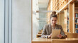 © Tania Zbrodko - Female university student studying on a tablet in a bright modern library, representing digital education and academic focus.