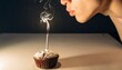 © Dedistudio - Person's mouth close up blowing out a single lit candle on a small frosted cupcake with smoke trailing upwards
