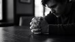 © Everlasting Dreams - A monochrome close-up focuses on tightly clasped hands with a ring on a dark wooden table, while a blurred man bows his head, conveying a somber visual feeling of heavy despair.