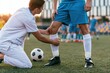 © gle - Sports doctor examining knee of injured soccer player on field. Medic assisting athlete with leg pain during football match. Professional medical help, injury treatment and recovery.
