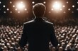 © whitestorm - Speaker addressing a large audience in a dimly lit auditorium with spotlights illuminating the stage.
