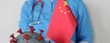 © Nadzeya - Medical professional holds a Chinese flag and a representation of the COVID-19 virus