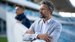 © Nataliya - Elegantly attired football manager standing confidently at the stadium overseeing a match, sports leadership concept, with copy space