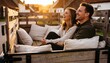 © Anna - Couple laughing in the back of a wooden truck at sunset. Young man and woman enjoying a rural road trip during golden hour. Romantic village getaway and lifestyle concept