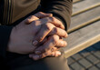 © Visual Verse - Two people sit side by side on a wooden bench outdoors, holding hands tightly with sunlight illuminating their embrace. Their fingers are intertwined.