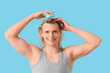 © Pixel-Shot - Young blonde man using hair scalp massager on blue background