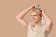 © Pixel-Shot - Young blonde man using hair scalp massager on beige background