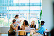 © we.bond.creations - Diverse business professionals brainstorming and discussing project data during a corporate meeting at a long table in a bright office