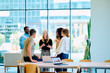 © we.bond.creations - Group of multi-ethnic colleagues engaged in discussion and teamwork, standing in a contemporary workplace with glass walls