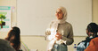 © peopleimages.com - Education, muslim woman and teacher in classroom at high school with study tips, learning or smile. Curriculum, person and female educator with students for teaching or academic support in lesson