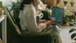 © shine.graphics - Woman working on laptop while relaxing in a cozy armchair surrounded by plants