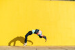 © VISTA by Westend61 - Acrobat jumping somersaults in front of yellow wall