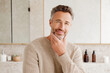 © kora studio - Healthy looking older man in his fifties with neatly styled beard, smiling confidently in modern bathroom setting. warm tones and natural materials create welcoming