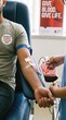 © Margarita Ratatosk - Man donating blood in clinic to support World Blood Donor Day. Medical nurse collecting blood in bag from volunteer donor for transfusion. Healthcare awareness, lifesaving charity concept.