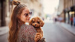 © Helga - Young woman holding small curly dog in city street, pet lifestyle portrait, dog owner love, urban walk, casual fashion, animal companionship, warm friendship and modern social medi