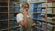© Krakenimages.com - Woman makeup artist touching under eye with finger while holding large powder brush among folded shirts on shelves in clothing store; focused care.